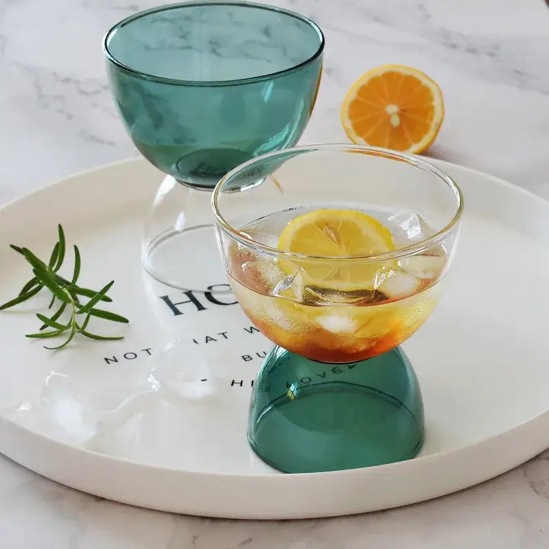 A clear glass dessert ice cream cup with a teal inverted base filled with ice and an orange slice