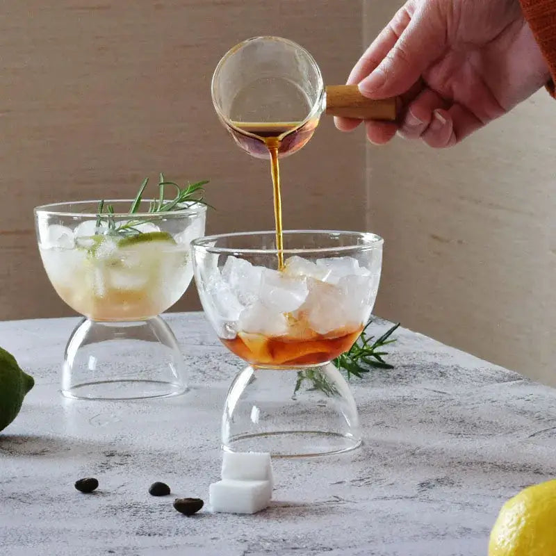 Clear glass cocktail coupe with wooden handle pouring amber liquid in modern colorful dessert ice cream cup set