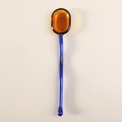 A decorbites glass dessert spoon set featuring a glossy amber glass spoon with a slender cobalt blue handle for dining room use