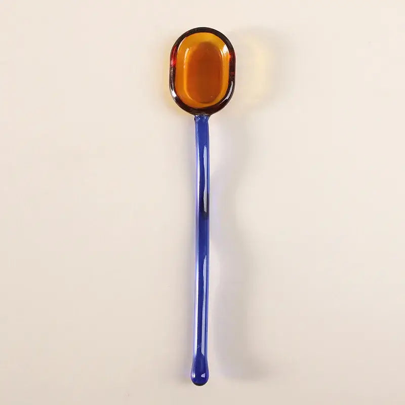A decorbites glass dessert spoon set featuring a glossy amber glass spoon with a slender cobalt blue handle for dining room use