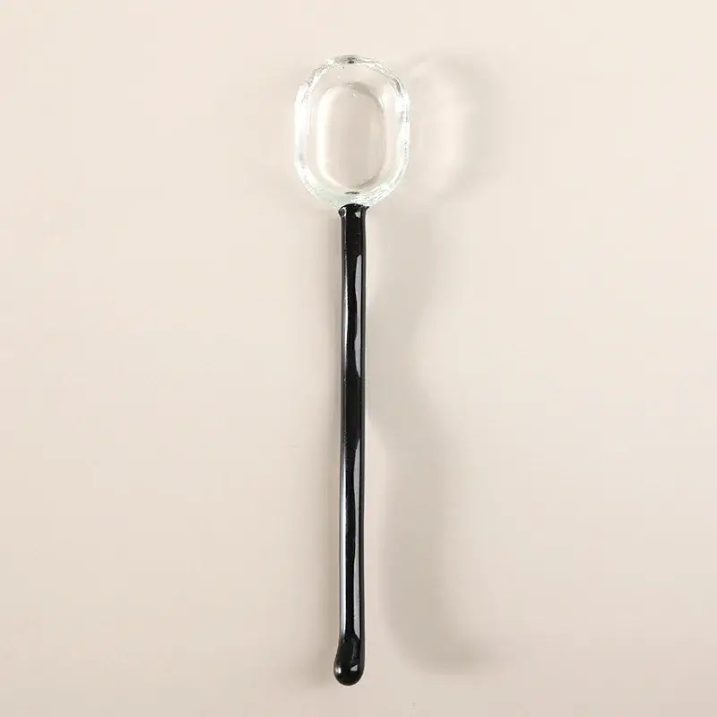 A sleek glass dessert spoon with a transparent bowl and glossy black handle from the decorbites dessert spoon set