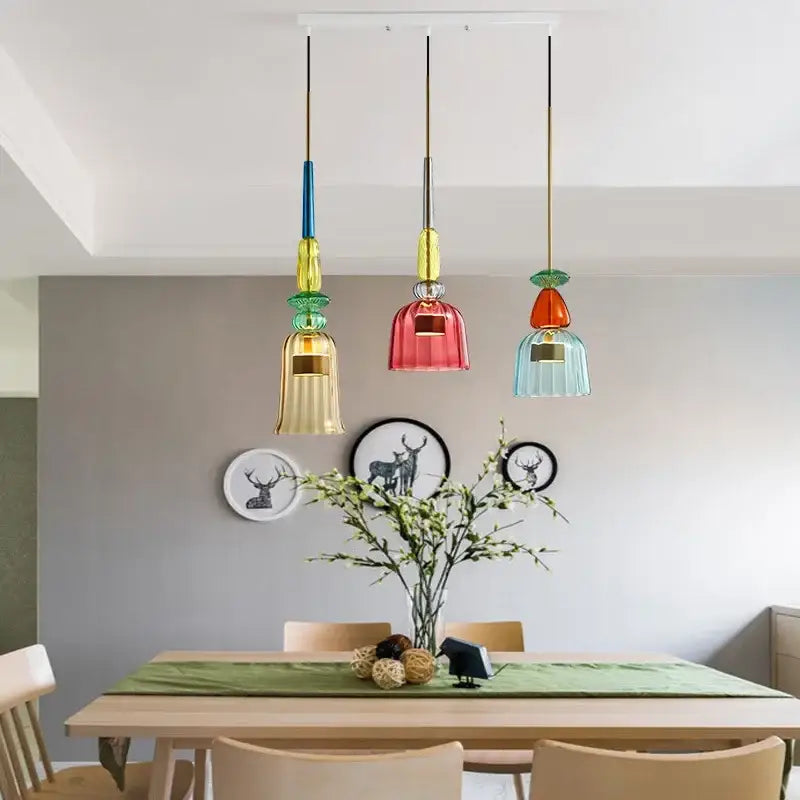 Three colorful glass led pendant chandeliers with metallic accents hang above a kitchen dining table