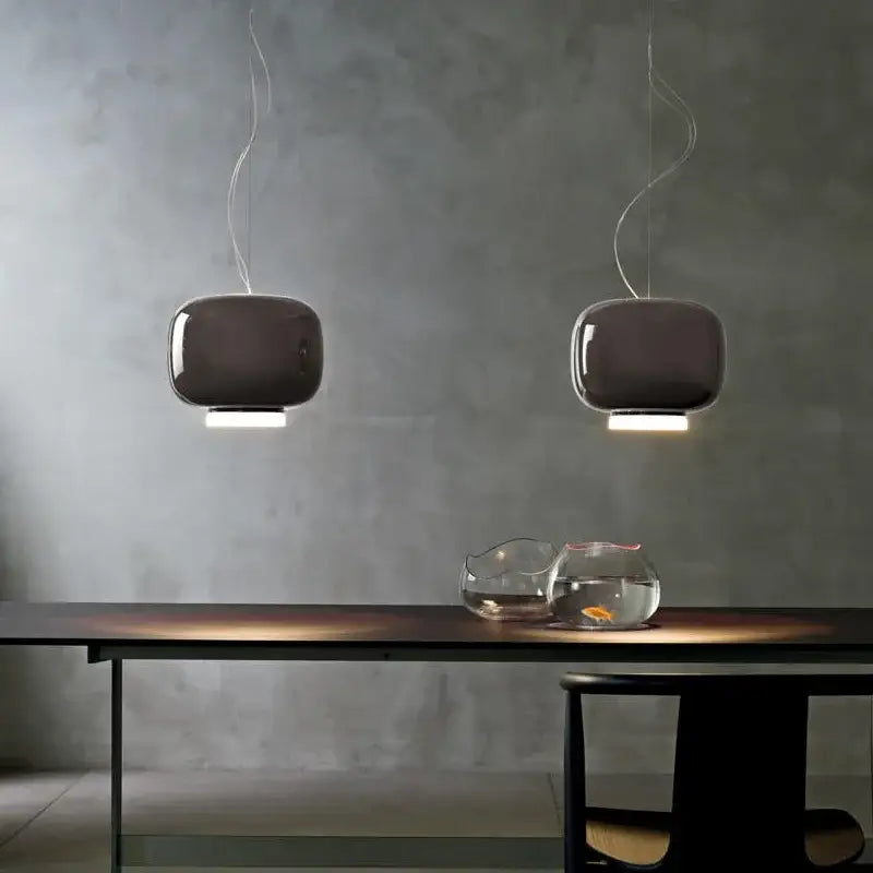Two sleek dark gray decorbites colorful glass pendant lights with curved glass shades hang above a dining table