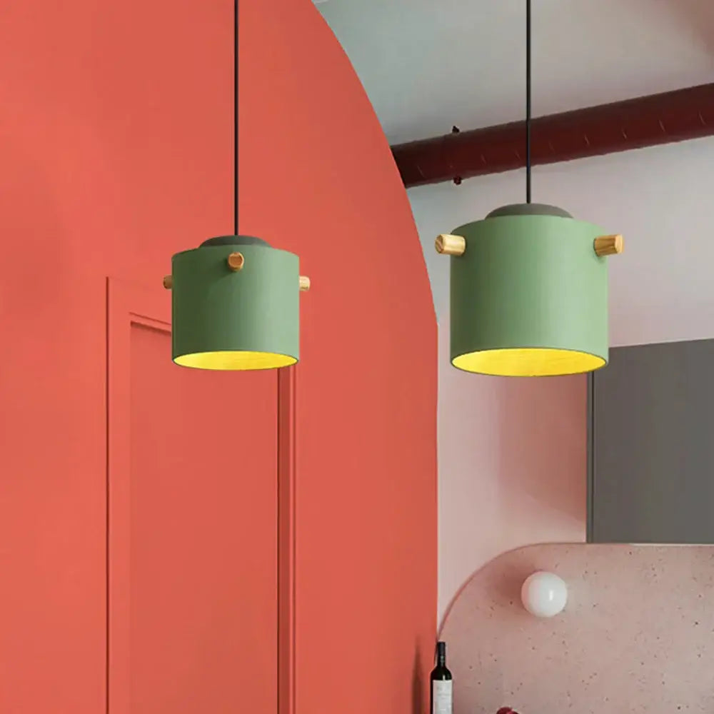 Two cylindrical green decorbites colorful led pendant lights with brass accents hang against a coral wall for dining room decor