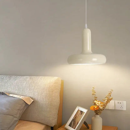 A sleek matte white painted aluminum pendant light with aluminum finish hangs above the bedside table
