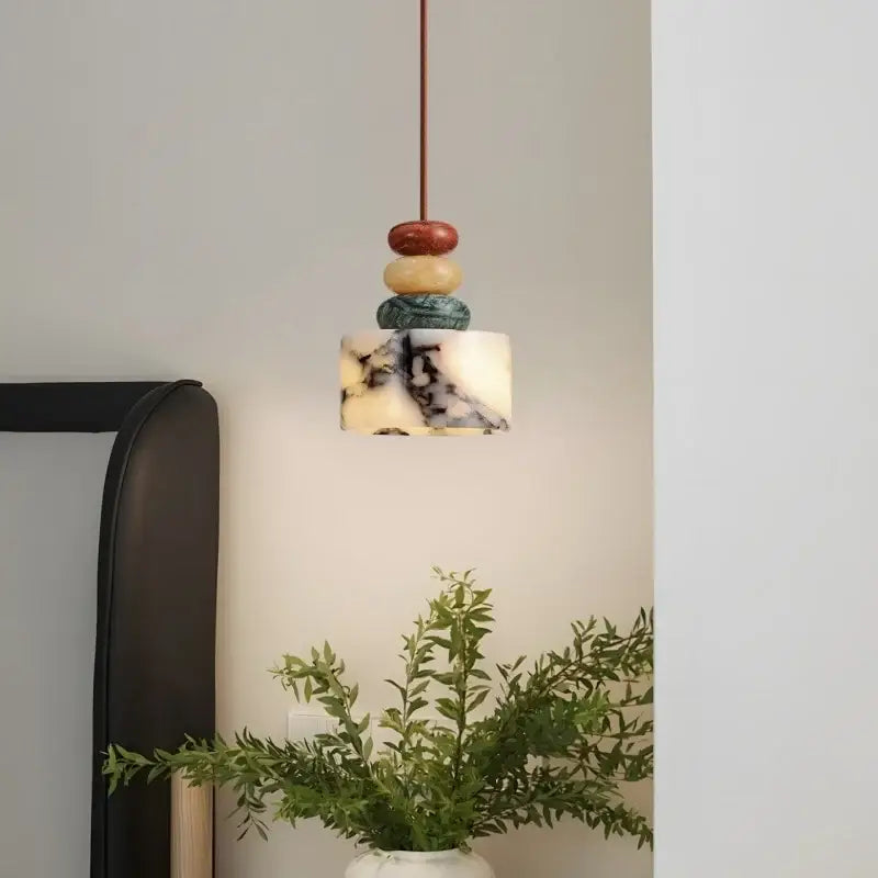 A modern pendant lamp with decorbites colorful stone orbs in red beige and teal above a white marble shade for dining decor