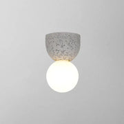Modern concrete bell wall-mounted light fixture with speckled gray finish and glowing white spherical bulb for bedroom sconce