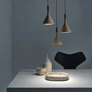 Three minimalist gray concrete pendant lights with conical shades hang on black cords for kitchen decorbites pendant lights