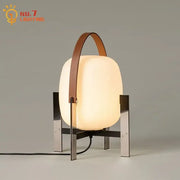 Modern cream designer metal glass table lamp with frosted body, sleek legs, and brown leather handle for bedroom decorbites