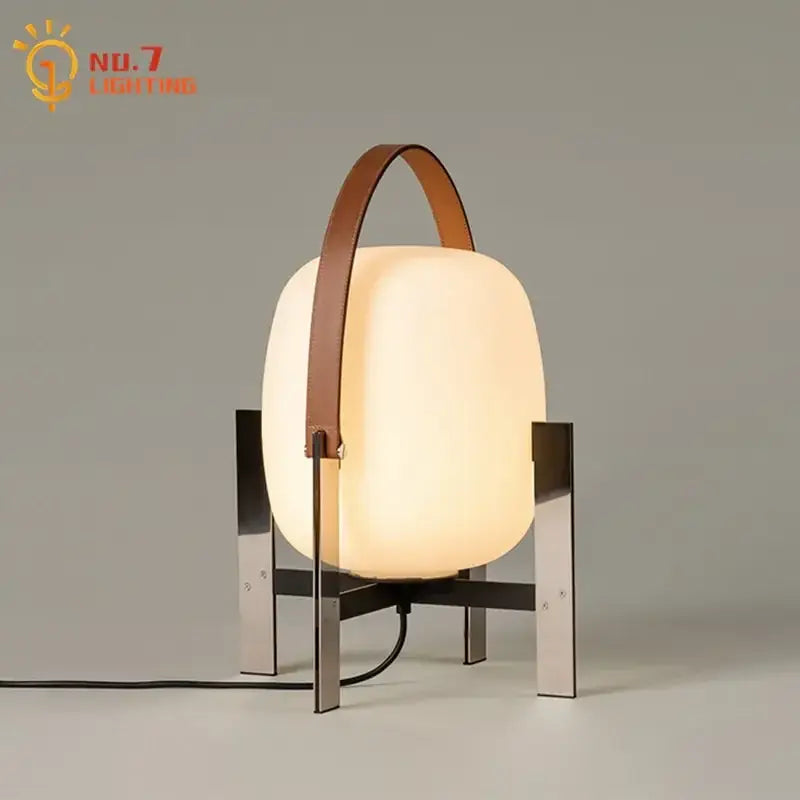 Modern cream designer metal glass table lamp with frosted body, sleek legs, and brown leather handle for bedroom decorbites