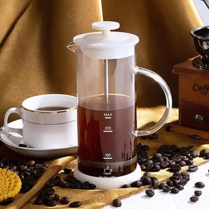 Modern cream glass french press coffee maker with white plastic lid and handle filled with dark coffee for hand foam mixer use