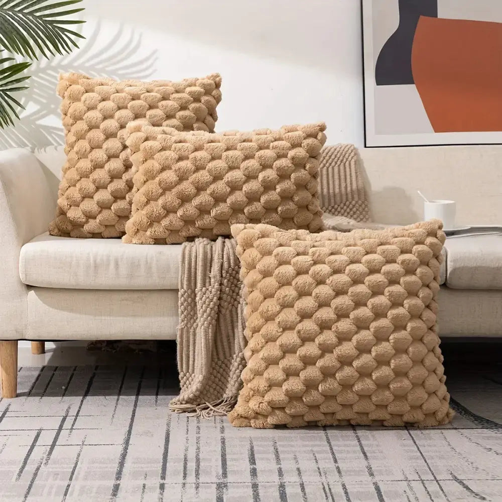 Three beige modern cream textured pom pom decorative pillow covers with raised pattern on a light-colored sofa