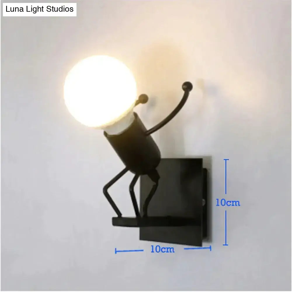 Black metal wall sconce shaped like a minimalism metal robot with outstretched arms holding a glowing bulb for bedroom use