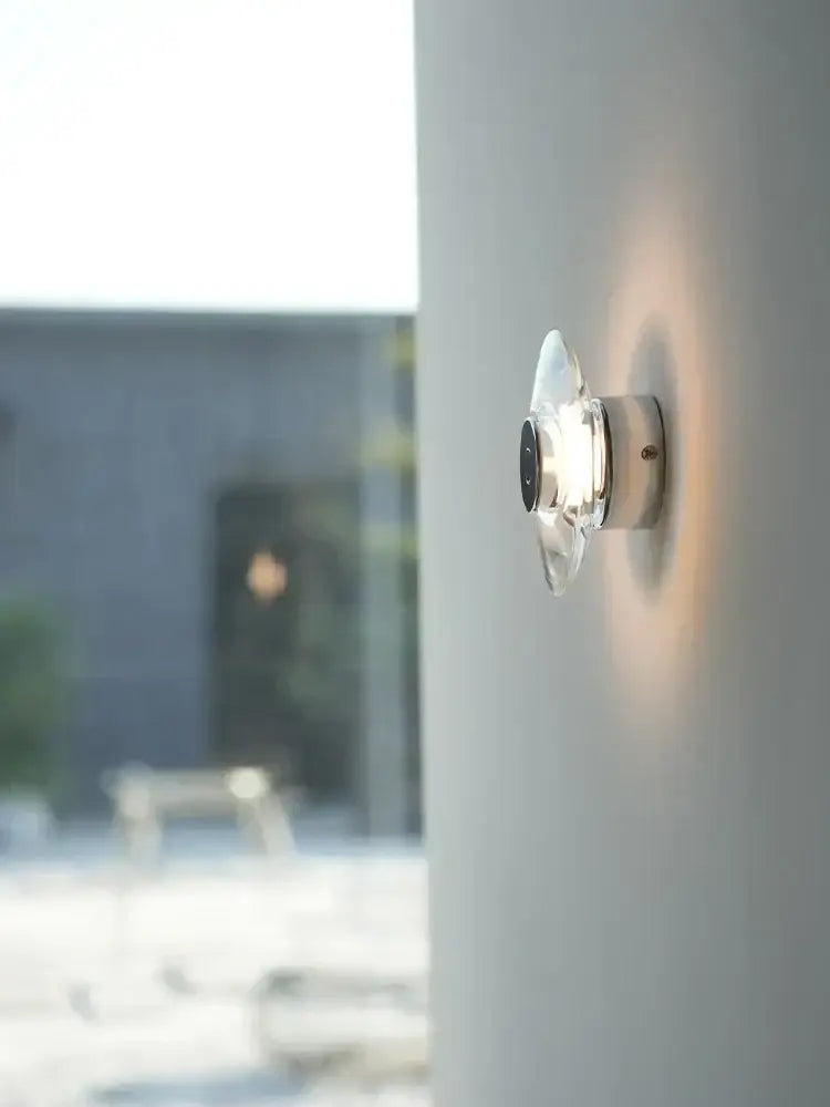 Modern crystal bedside wall lamp with clear glass, chrome base, and black accent emitting warm ambient light for decorbites