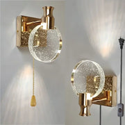 Gold wall lamp featuring a clear circular crystal glass globe filled with sparkling particles for modern bedroom decorbites crystal glass