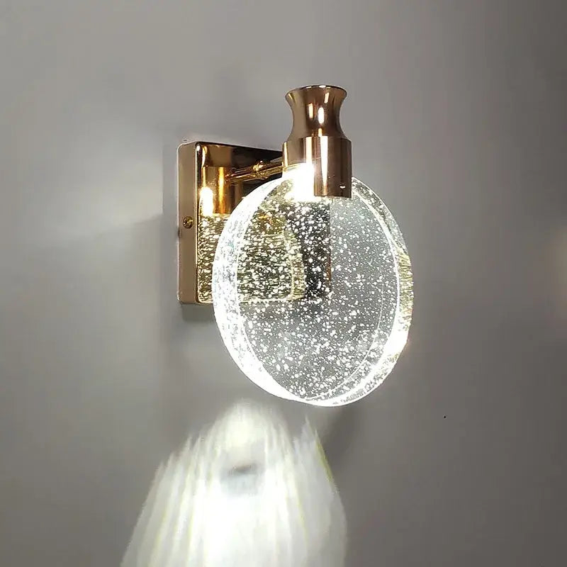 A modern wall lamp with a gold-toned metal base and decorbites crystal glass globe for warm bedroom lighting