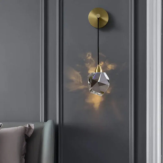 A modern crystal golden wall sconce with faceted clear glass shade and gold-toned metal fixture by decorbites