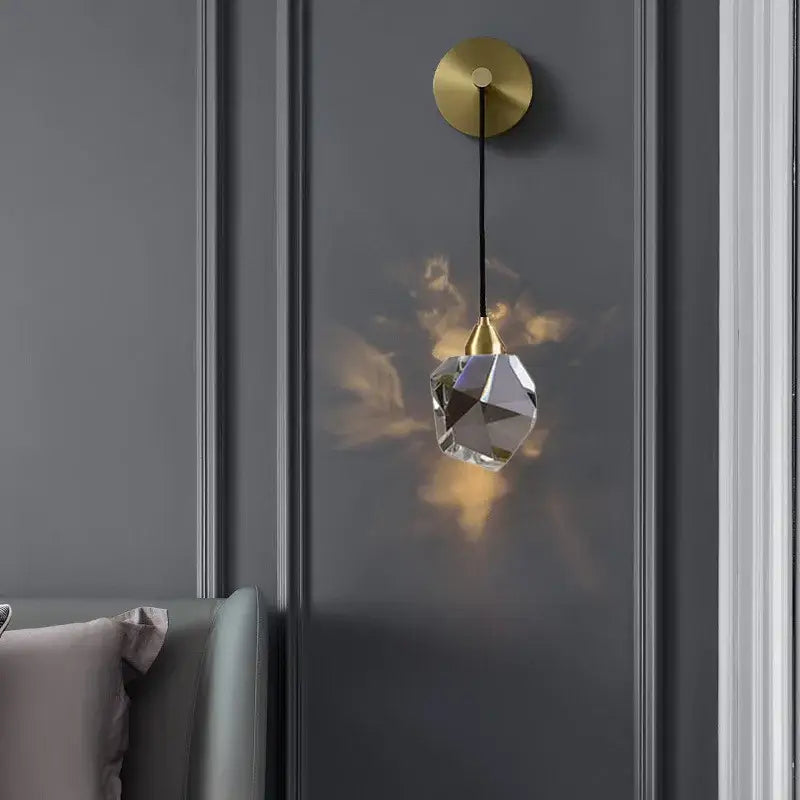 A modern crystal golden wall sconce with faceted clear glass shade and gold-toned metal fixture by decorbites