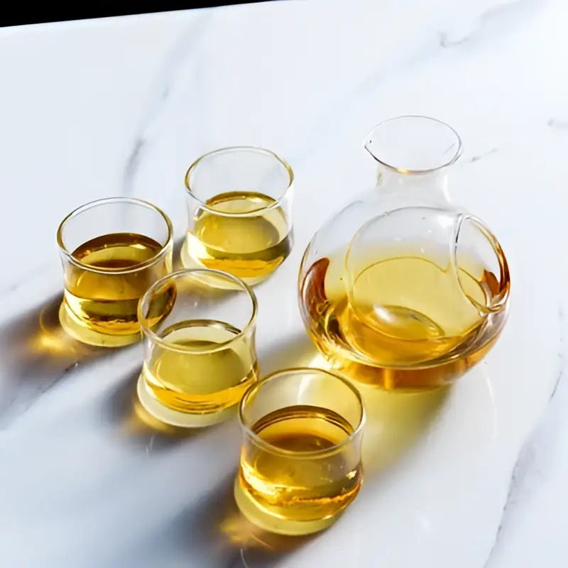 Modern crystal sake ice jug with clear glass carafe and four golden liquid-filled tumbler glasses by decorbites crystal sake