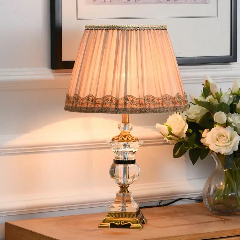 Elegant decorbites crystal table lamp with gold-toned base and pleated peach fabric shade with cream lace trim