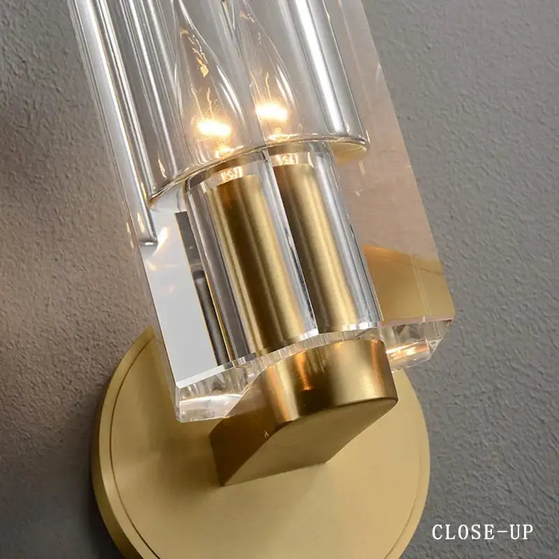 A modern crystal wall lamp with clear faceted glass tubes and brushed brass base for bedroom decorbites wall lamp