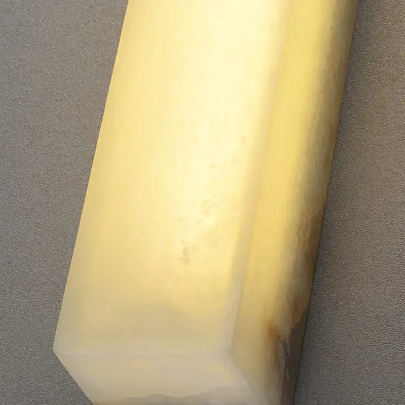 A smooth translucent yellowish-white cuboid marble led wall lamp by decorbites for modern bedroom dimmable lighting decor