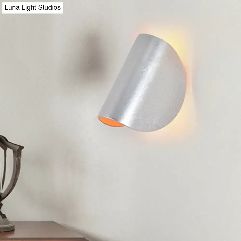 Modern curved gold wall sconce light with silver metallic half-cylinder design and warm orange glow for ambient bedroom lighting