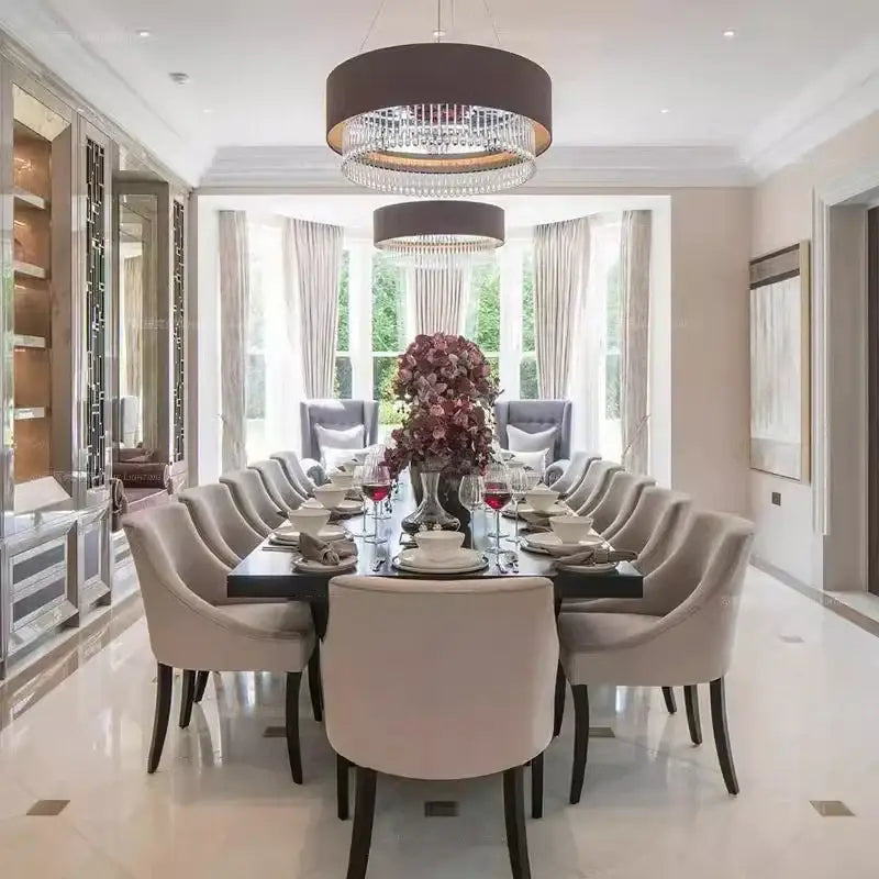 A modern dark gray decorbites crystal pendant chandelier illuminating a luxurious dining table with beige chairs and white porcelain dinnerware