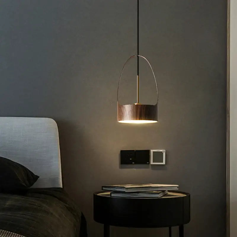 A modern copper-toned decorbites led wood grain pendant light with minimalist design above a dark bedside table