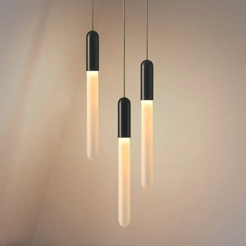 Three modern pendant lights with black matte tops and warm glowing shades in decorbites luxe gold tube chandelier design