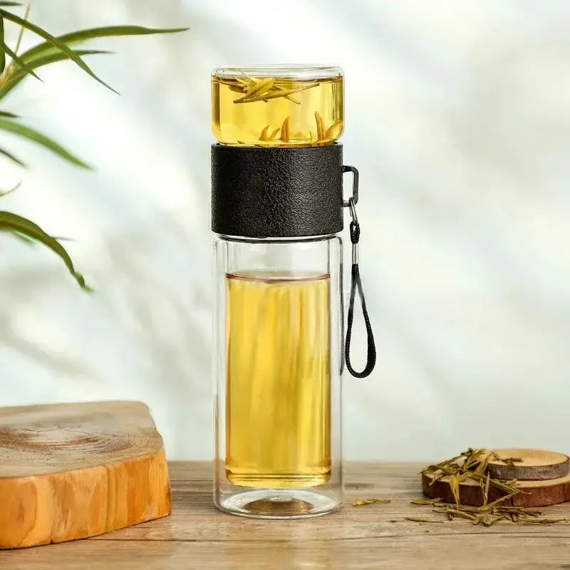 Modern double layer glass tea infuser bottle with black grip and strap filled with golden brewed tea for kitchen use