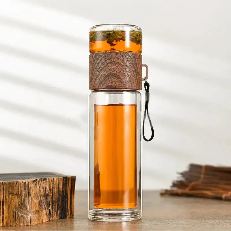 Modern double layer glass tea infuser bottle with amber tea, dark wood lid, and black strap for kitchen use