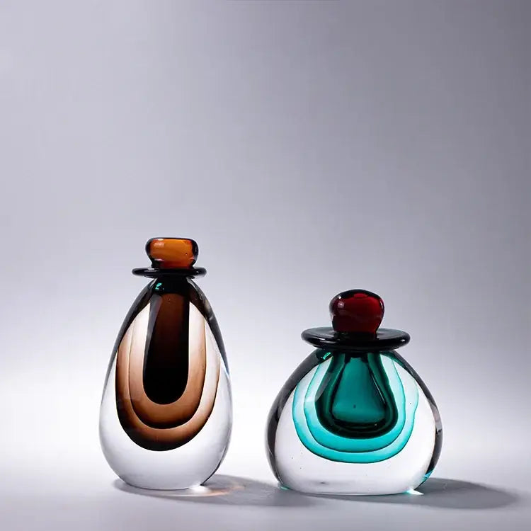 Two elegant glass perfume bottles with double stained glass design featuring amber black and teal green layers in a vase