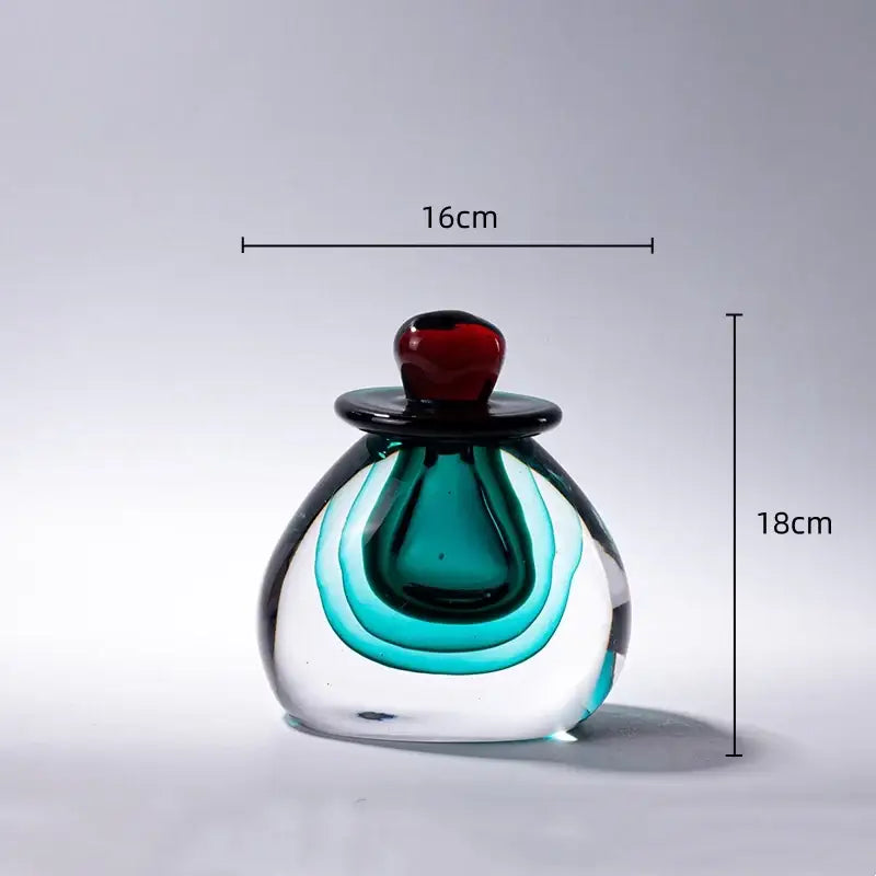 A translucent glass perfume bottle with double stained glass teal and black swirls and a glossy red cap