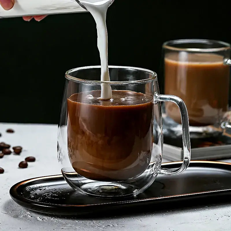 Modern double wall glass coffee cup set featuring a clear double wall glass coffee cup filled with espresso poured from a white pitcher