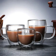 Set of three clear double wall glass coffee cups with handles filled with brown liquid for espresso use