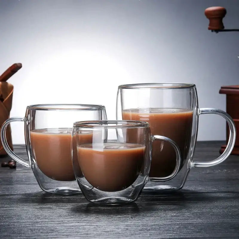 Set of three clear double wall glass coffee cups with handles filled with brown liquid for espresso use