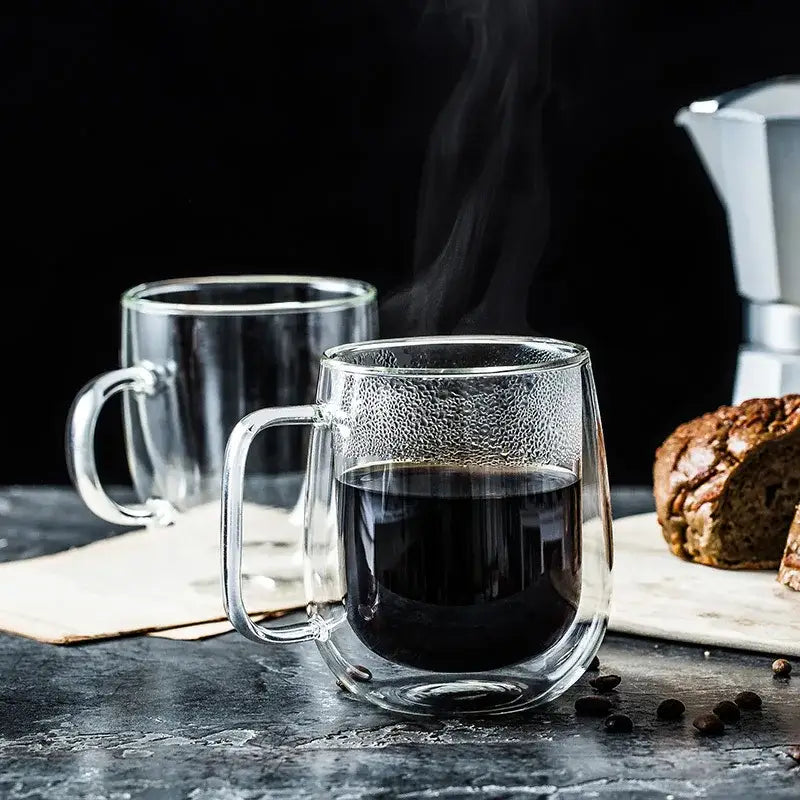 Modern double wall glass coffee cup with textured surface and clear handle filled with steaming dark espresso