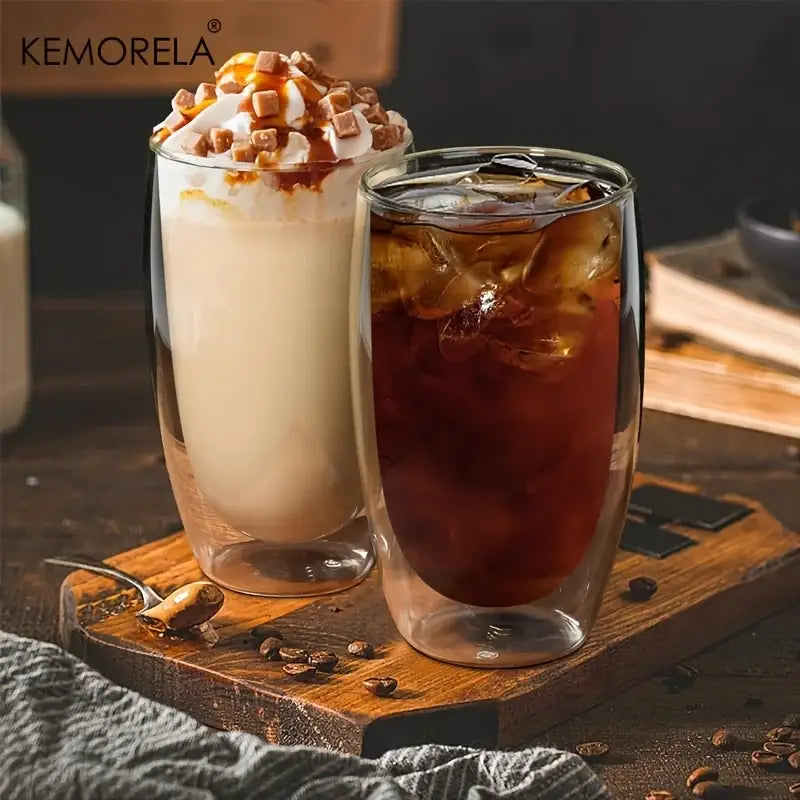 Two modern double wall glass coffee mugs one with iced coffee and one with caramel milkshake topped with whipped cream