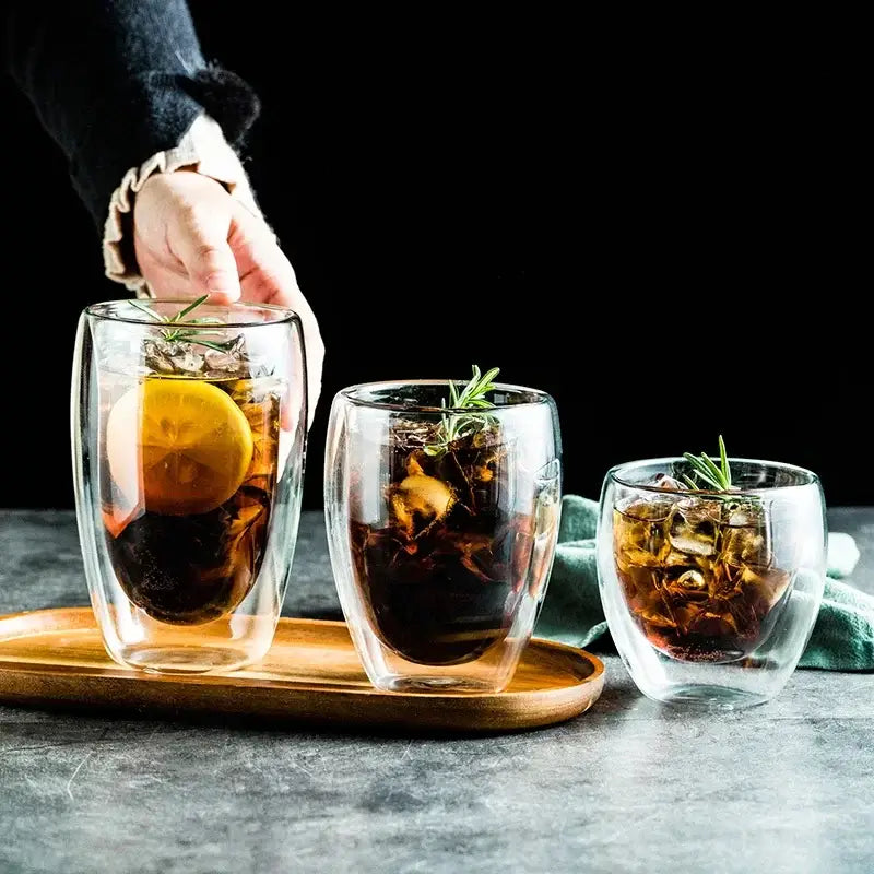 Set of three clear modern double wall glass coffee mugs with ice lemon slices and rosemary for kitchen use
