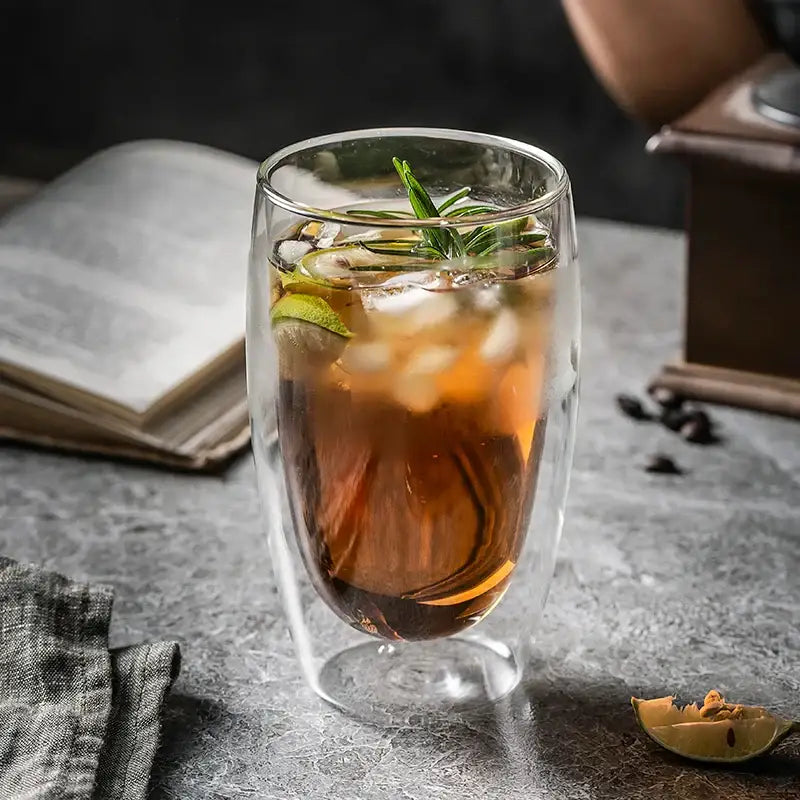 Modern double walled transparent glass cup with iced tea garnished with rosemary and lime slices in a glass cup