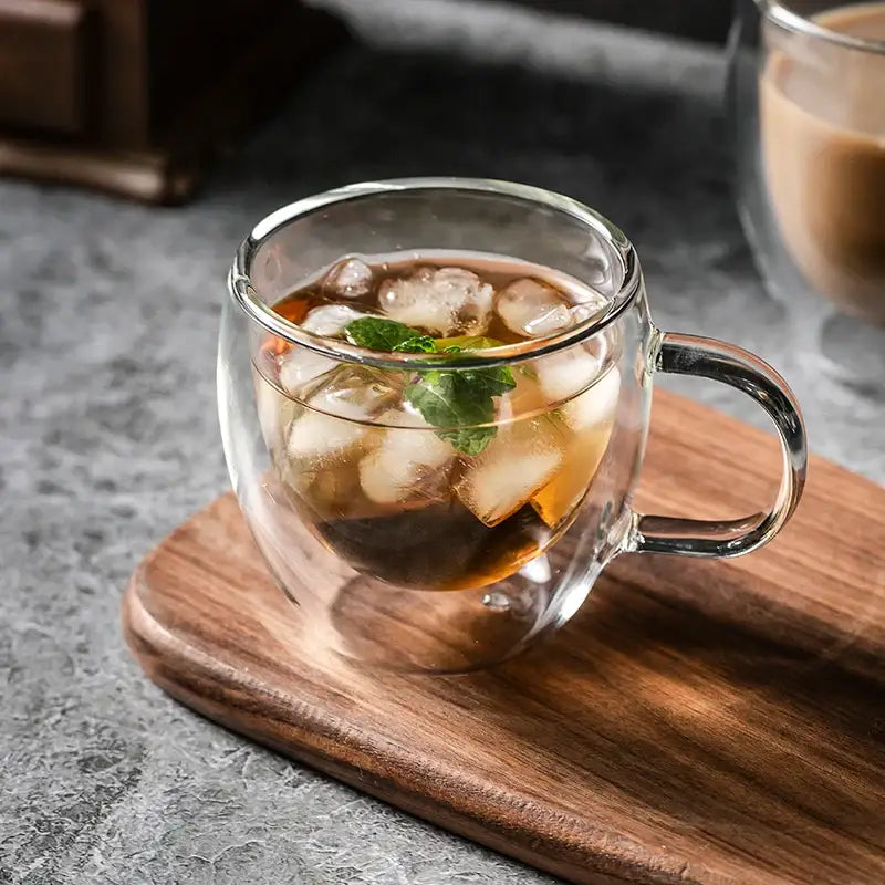 Modern double walled transparent glass cup with handle filled with iced tea and mint leaves as a glass cup