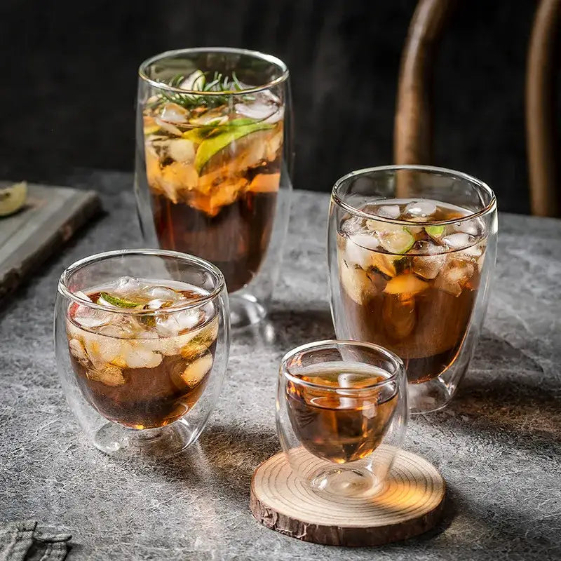Set of clear modern double walled transparent glass cups with ice and garnishes for kitchen and dining use