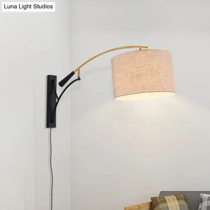 Beige linen textured modern drum shade wall lamp in flaxen coffee mounted on a curved brass arm with black bracket