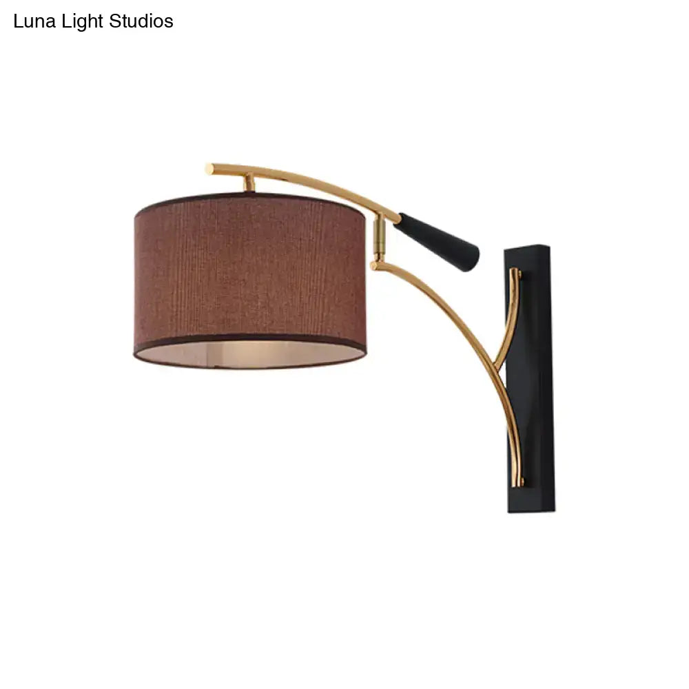 Modern drum shade wall lamp with a flaxen coffee textured fabric shade and curved gold-toned metal arm for bedroom use