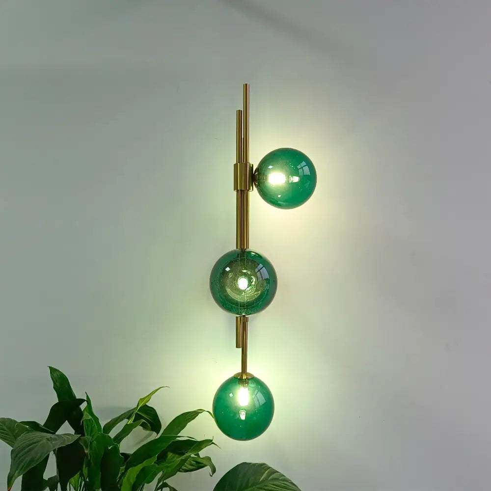 Modern wall lamps featuring three stacked emerald green glass globes with brass-toned arms for elegant decorbites green white style