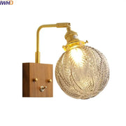 Brass-finished wall lights with spherical etched glass copper led shade featuring leaf patterns and wooden base plate