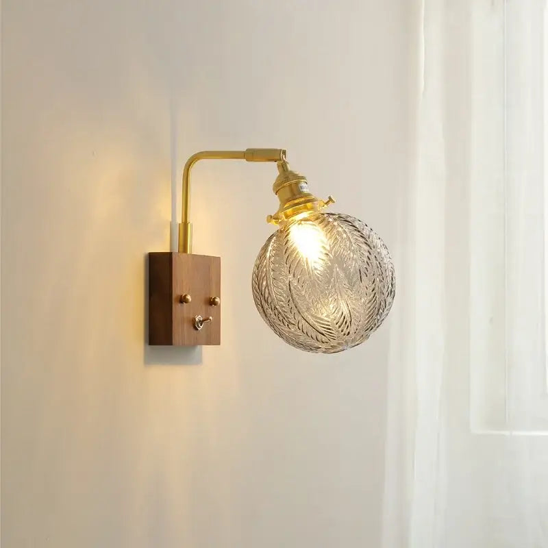 Brass-finished wall lights with wooden base and intricately etched clear glass copper led globe for bedroom sconce