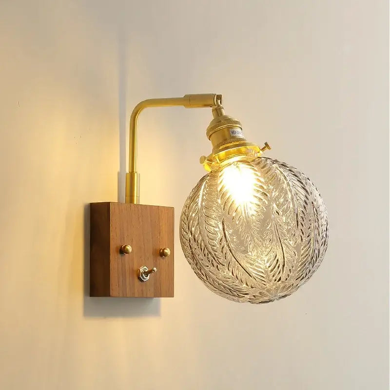 A vintage-style wall light with a brass-finished arm and ornate etched glass copper led shade for bedroom sconce
