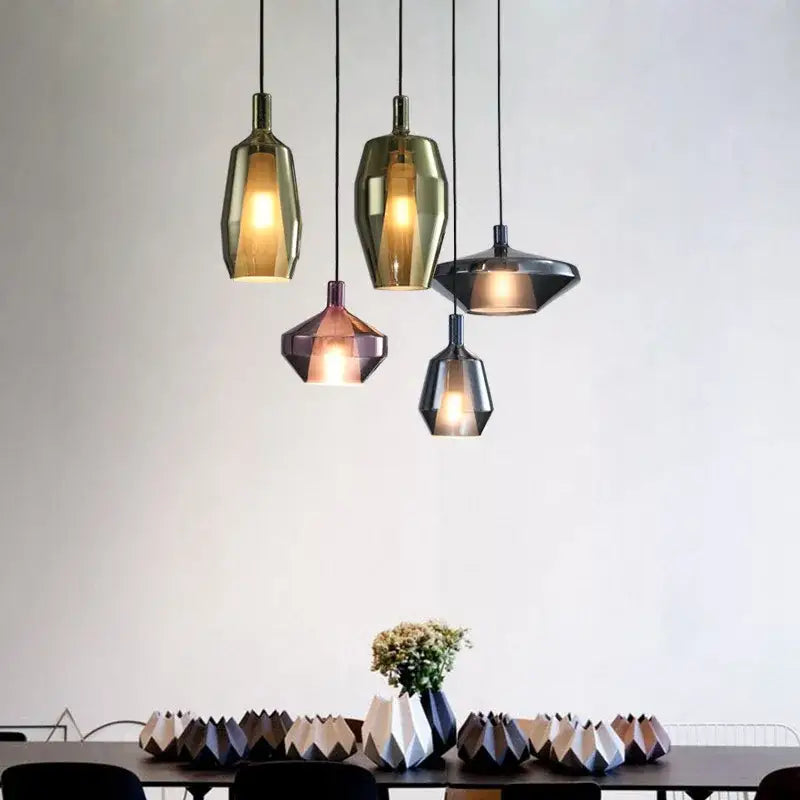 Five modern faceted glass pendant lights in gold bronze and dark gray hang above a dining table for home art decor